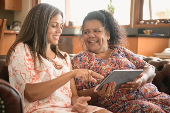 A woman and her mother engrossed in a tablet while sitting on a couch.