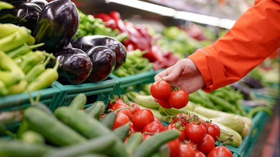 A person choosing a red tomatoes from the fresh produce section.