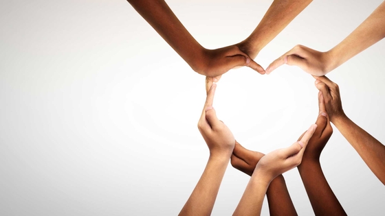 Hands of several people forming a heart shape, with outdoors background