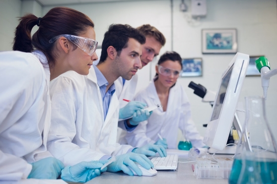 A group of scientists in lab coats observing a computer screen in a research laboratory.
